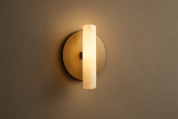 A modern wall sconce on a textured wall, warm ambient glow, minimalist luxury interior, matte brass or alabaster material, elegant soft lighting, balanced composition, 1:1 ratio.